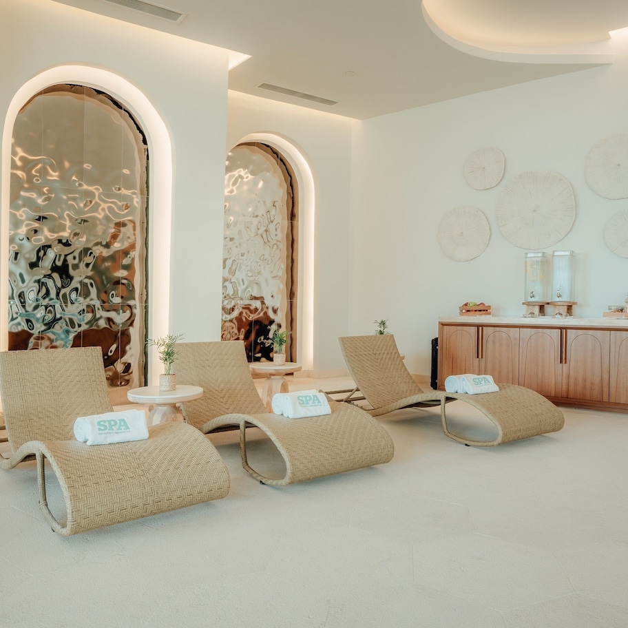 A spa room with three lounge chairs, a wooden cabinet, and wall-mounted clocks.