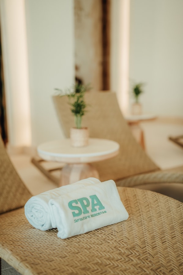 Una toalla enrollada con el texto "SPA" y "Sensations Understar" sobre una silla de mimbre.