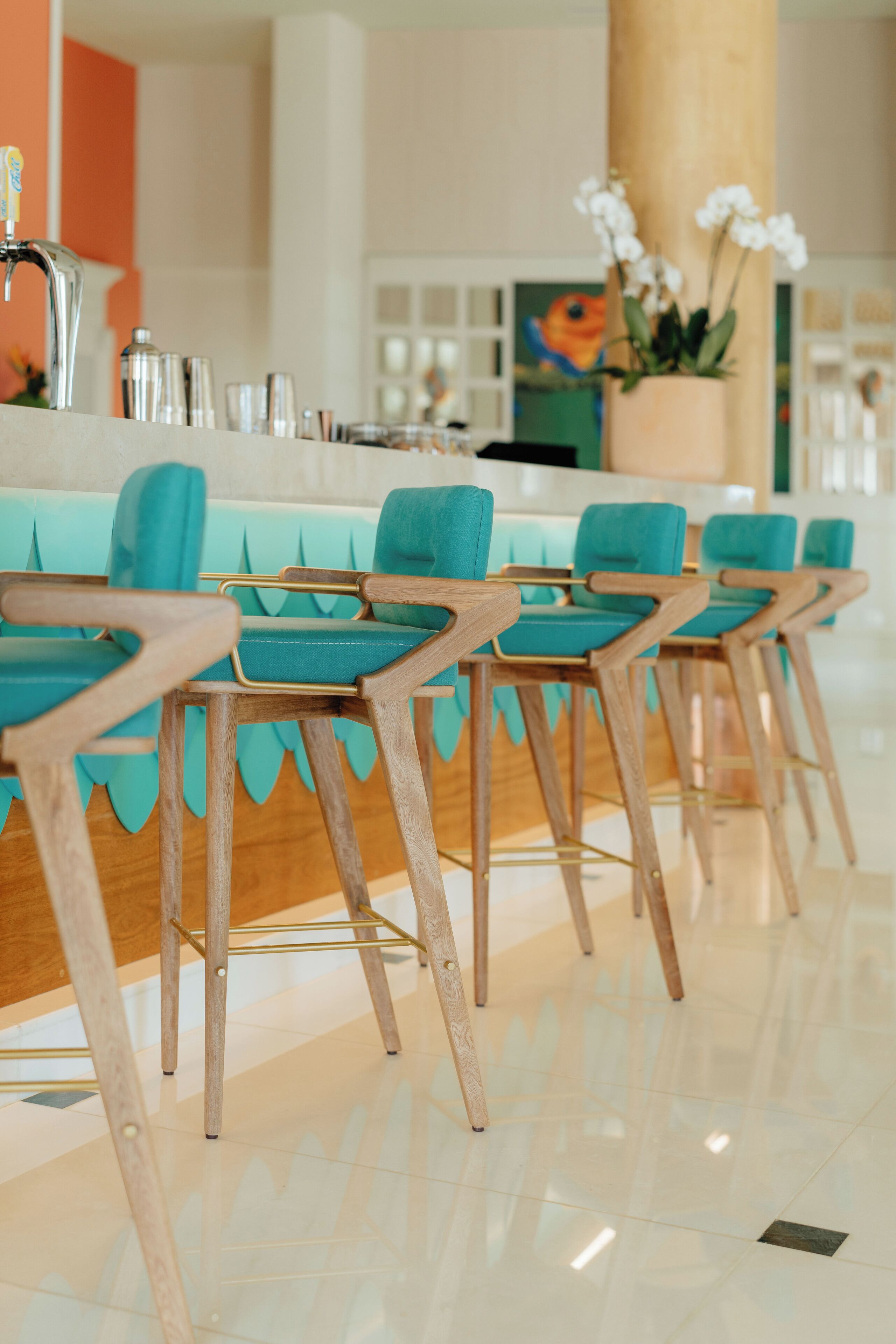 Une rangée de chaises de couleur turquoise, avec des montures en bois, et un comptoir blanc doté d’un robinet.