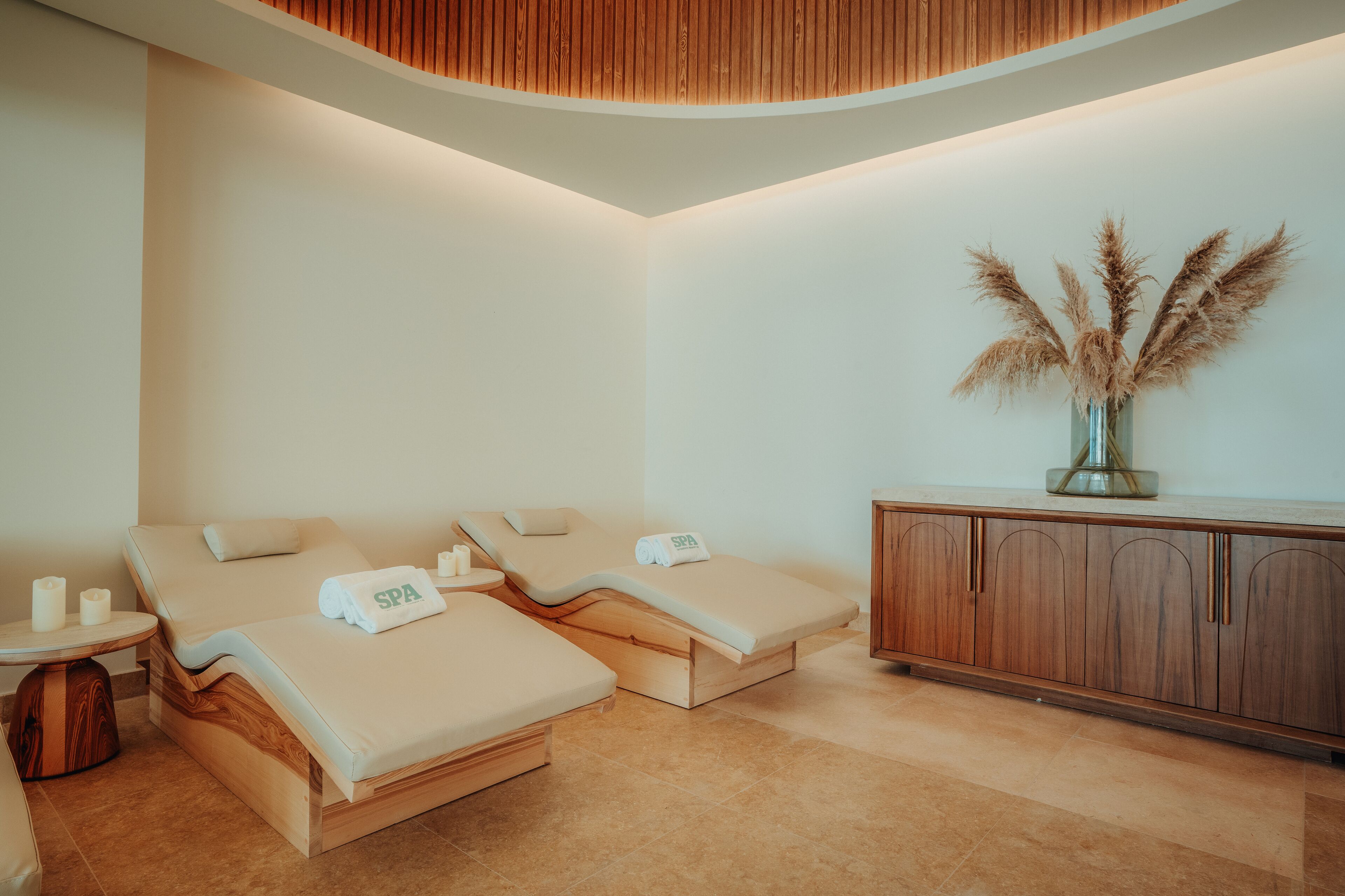 Un cuarto de spa con dos camillas de masaje, un armario de madera y un florero con plantas secas.