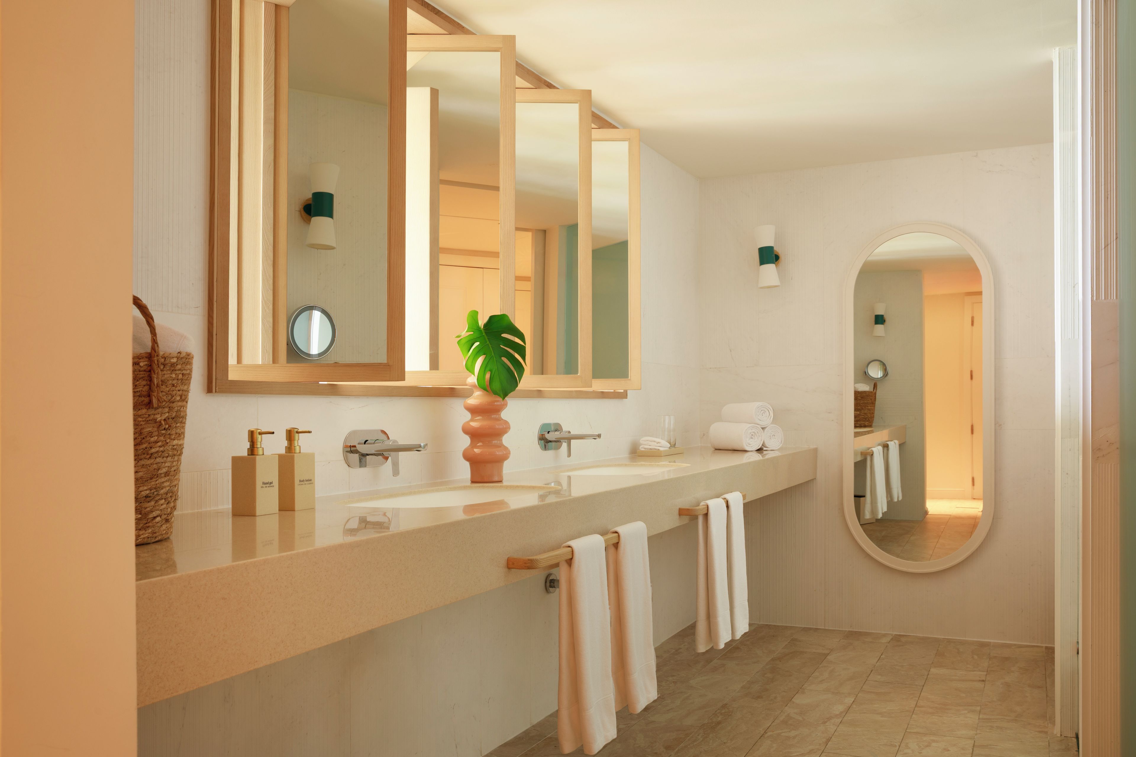 Un baño moderno con un espejo grande, dos lavamanos, una planta en maceta y toallas.