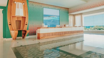 Un moderno vestíbulo de hotel con un mostrador de recepción, un ventanal con vistas al océano y un suelo estampado.