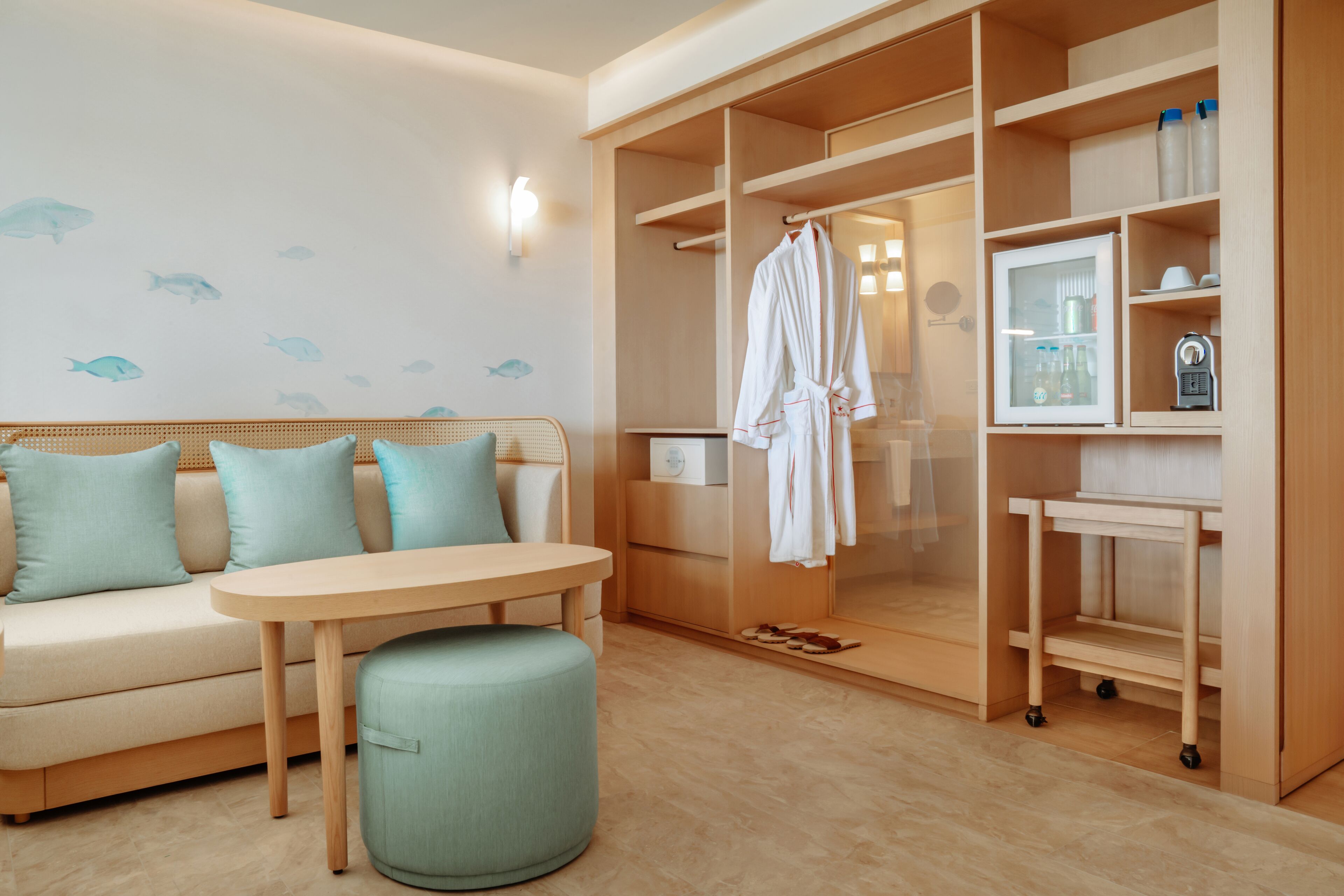 A modern hotel room with a sofa, ottoman, wooden wardrobe, and a small table.
