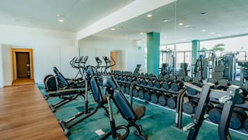 Un gimnasio con equipo de ejercicio, estantes para pesas y piso de madera.