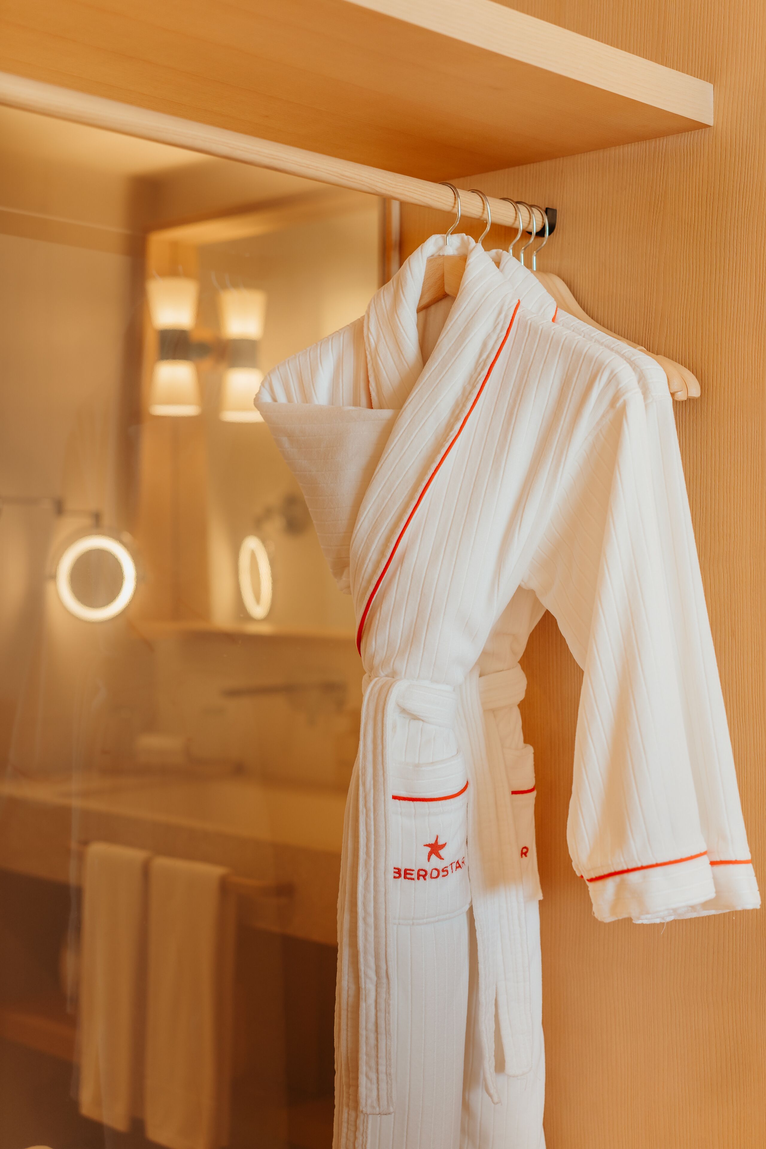 Ein weißer Bademantel hängt an einem Holzgestell in einem Badezimmer mit Spiegel und Handtuchhalter.