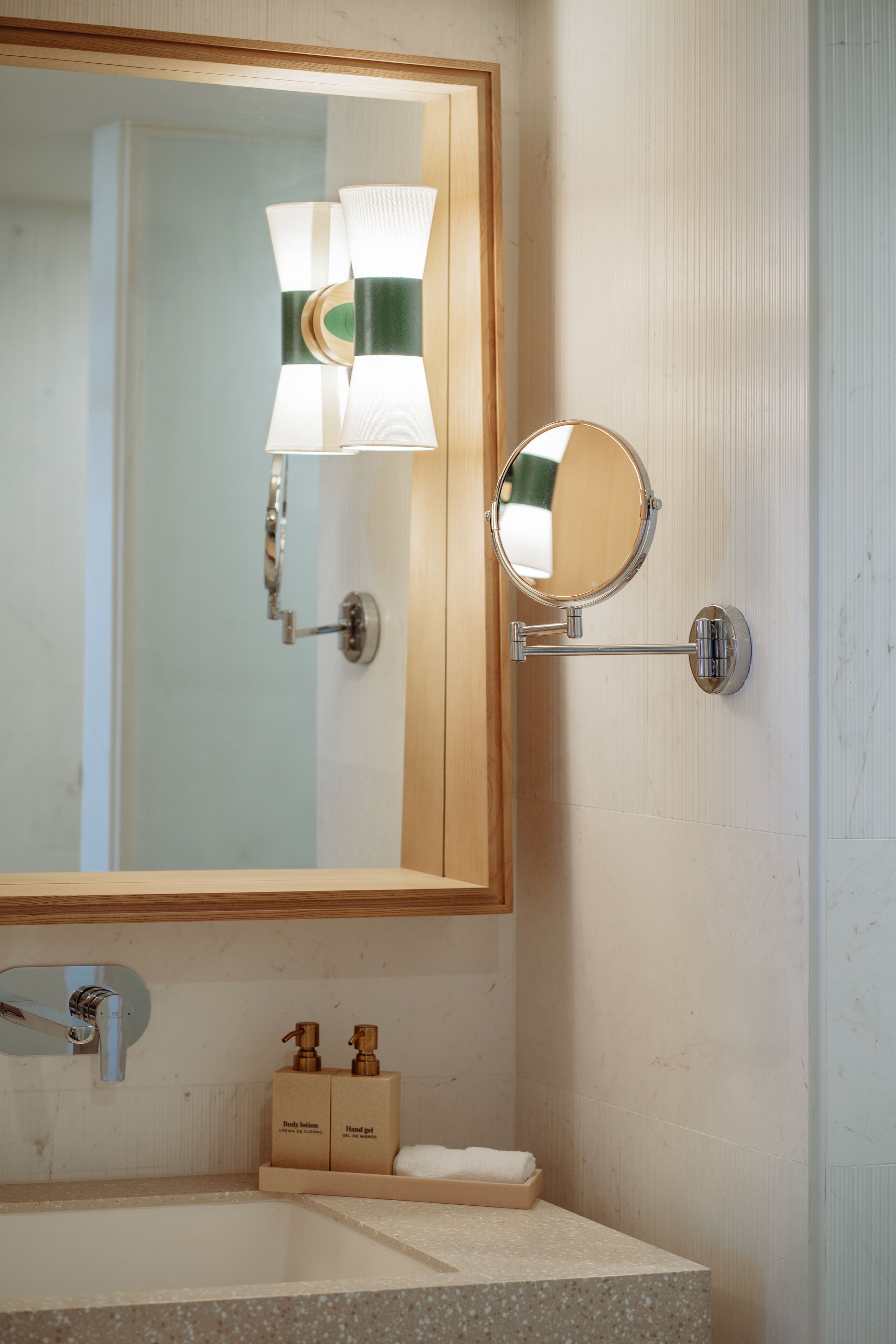 A bathroom with a large mirror, wall-mounted light fixtures, a sink, and two soap dispensers.
