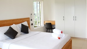 A neatly made bed with white and dark pillows, a wooden headboard, and a small desk with a chair. - Lagati Residence (Mahé Island)