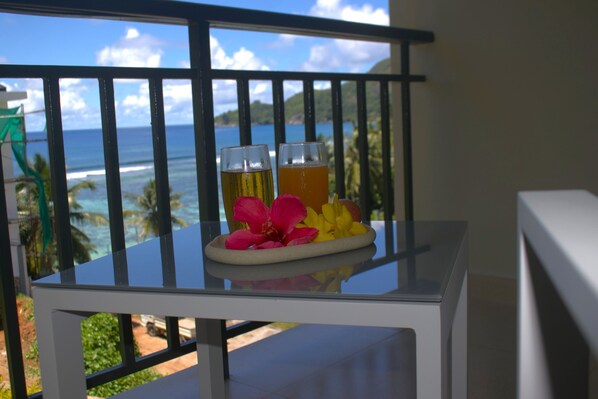A balcony with a glass table holding two glasses of beer and tropical flowers.