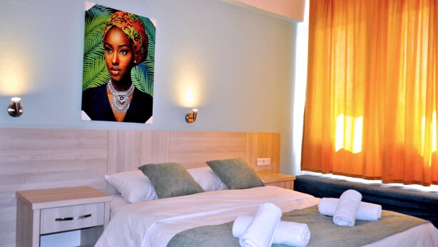A hotel room with a bed, a nightstand, a wall-mounted picture, and a window with curtains. - Native Hotel (Fethiye)