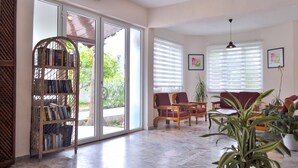 A spacious living area with a sliding glass door leading to a balcony, a wooden bookshelf, and several seating options. - Native Hotel (Fethiye)