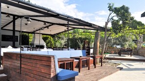 An outdoor seating area with wooden benches and tables, a covered section with a grill, and a stone wall in the background. - Native Hotel (Fethiye)