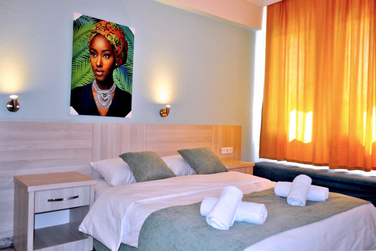 A hotel room with a bed, a nightstand, a wall-mounted picture, and a window with curtains.