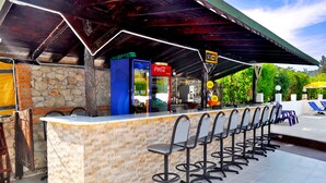 An outdoor bar area with a stone wall, a Coca-Cola refrigerator, and a row of bar stools. - Native Hotel (Fethiye)