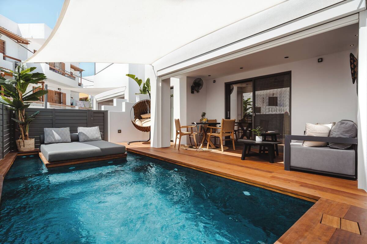 A modern poolside area with a built-in seating area, a dining table, and a small kitchen setup.