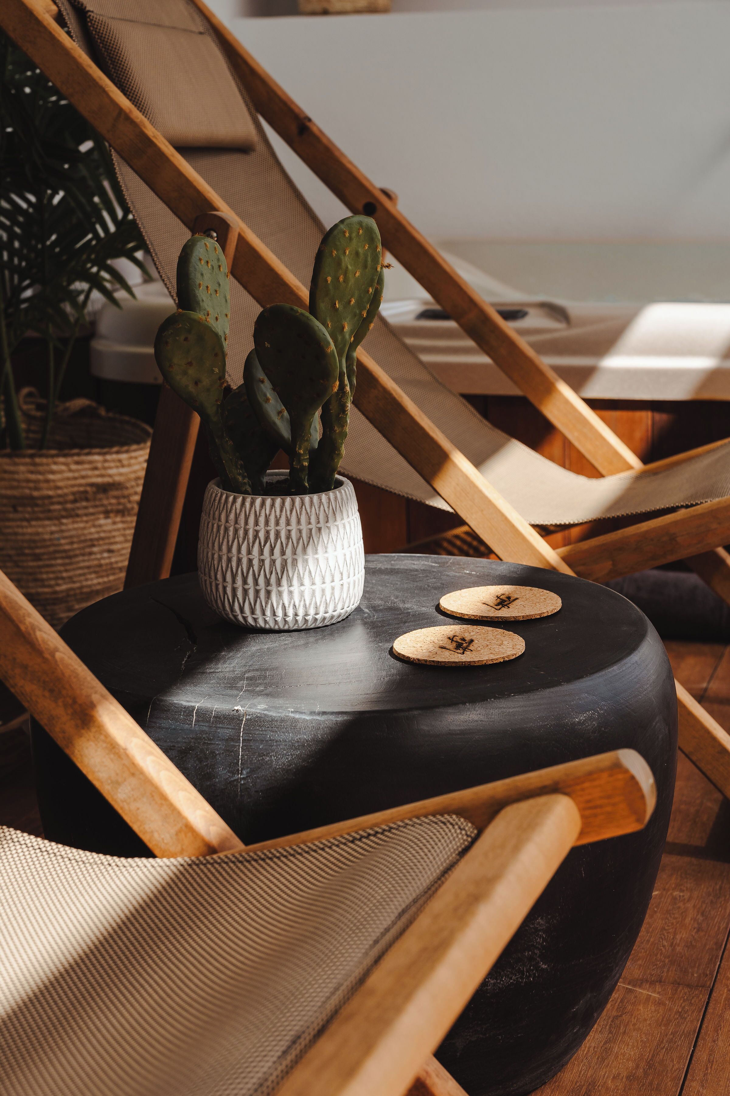 A wooden chair with a woven basket and a potted cactus plant on a round black table.