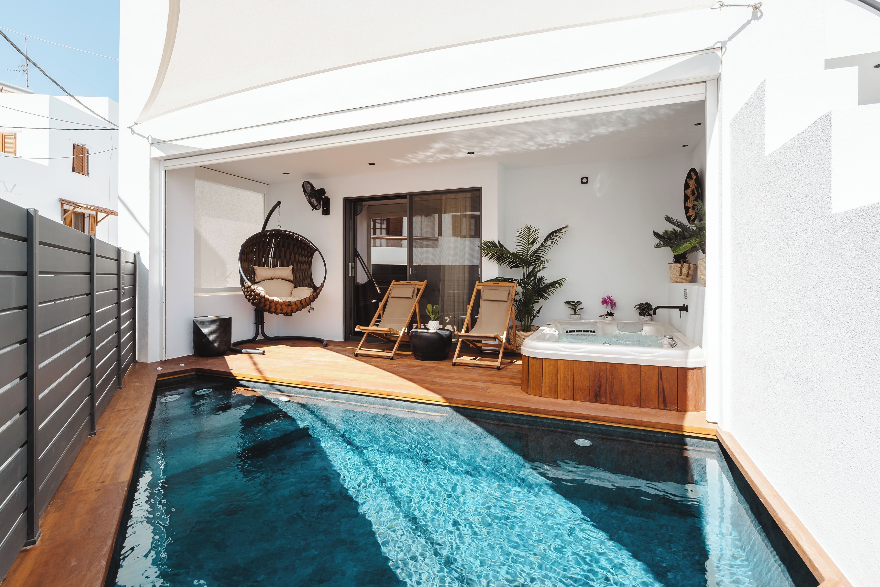 A modern outdoor pool area with a hot tub, lounge chairs, and a hanging chair.