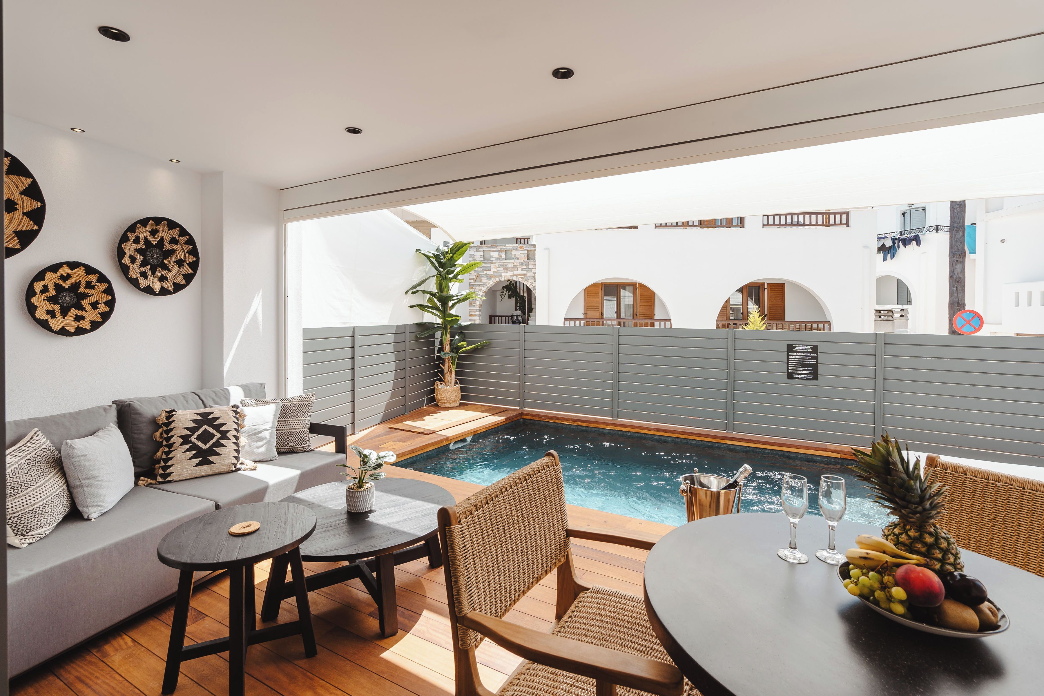 Un'area esterna moderna con posti a sedere, una piscina, un divano e un tavolo con frutta e bicchieri.