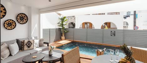 Un'area esterna moderna con posti a sedere, una piscina, un divano e un tavolo con frutta e bicchieri.