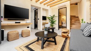 Ein modernes Wohnzimmer mit Flachbildfernseher, Holzbalken, einem runden Couchtisch und einer Couch mit gemusterten Kissen.