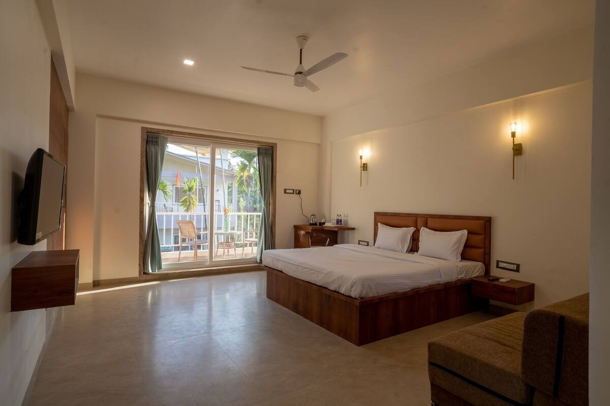 A bedroom with a large bed, a ceiling fan, a TV mounted on the wall, and a sliding glass door leading to an outdoor area.