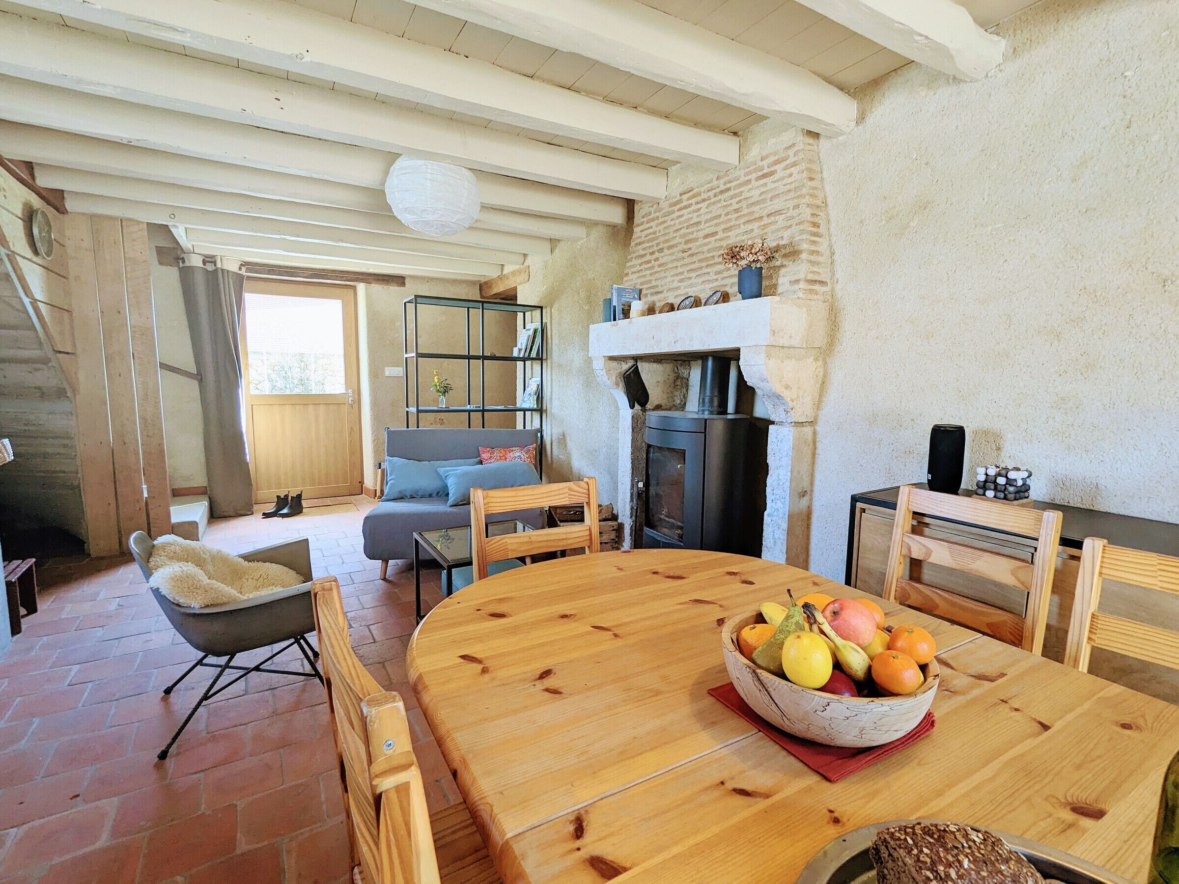 A cozy living room with a fireplace, a wooden dining table with fruit, and a comfortable seating area.