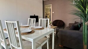 A dining area with a white table and chairs, a dark-colored sofa, and a potted plant. - 2-Room Apartment Near Sea, Air Conditioning, 4 Sleeps (Argelès-sur-Mer)