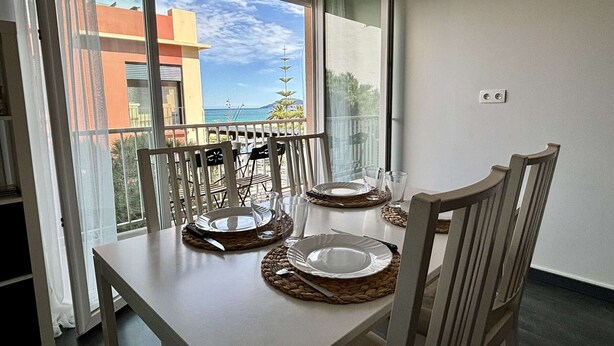 A dining table with four chairs, two glassware items, and two plates on woven placemats. - 2-Room Apartment Near Sea, Air Conditioning, 4 Sleeps (Argelès-sur-Mer)