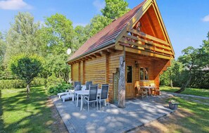 Una cabaña de madera con techo inclinado, un patio con mobiliario exterior y un entorno de jardín.