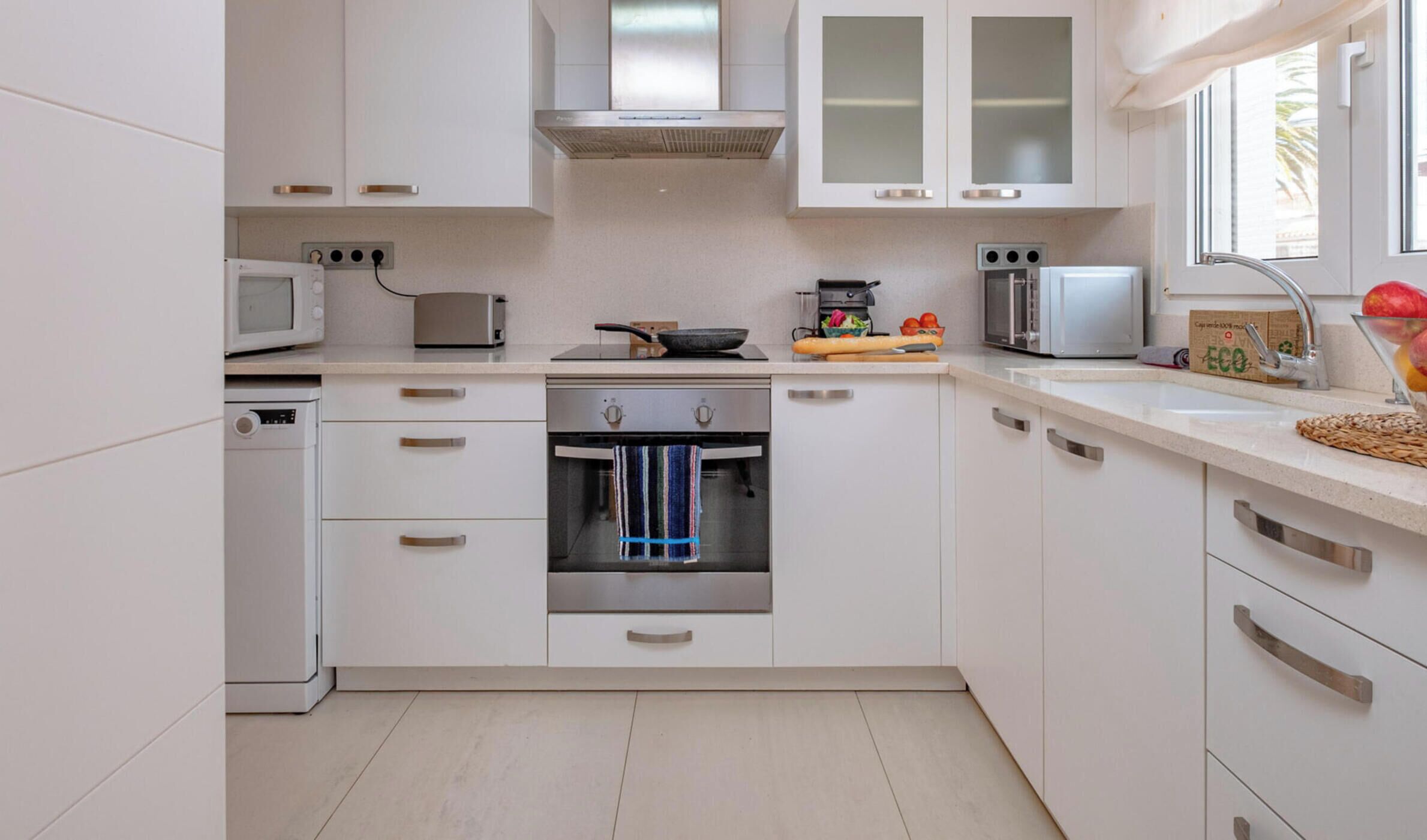 A modern kitchen with white cabinets, stainless steel appliances, and a window providing natural light.