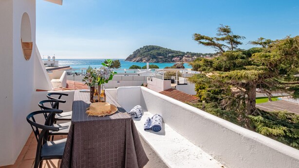 A balcony with a table, chairs, and a view of the sea and a hill. - Beachfront Family Retreat with Stunning Sea Views in Palamós (Palamós)