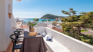 A balcony with a table, chairs, and a view of the sea and a hill.
