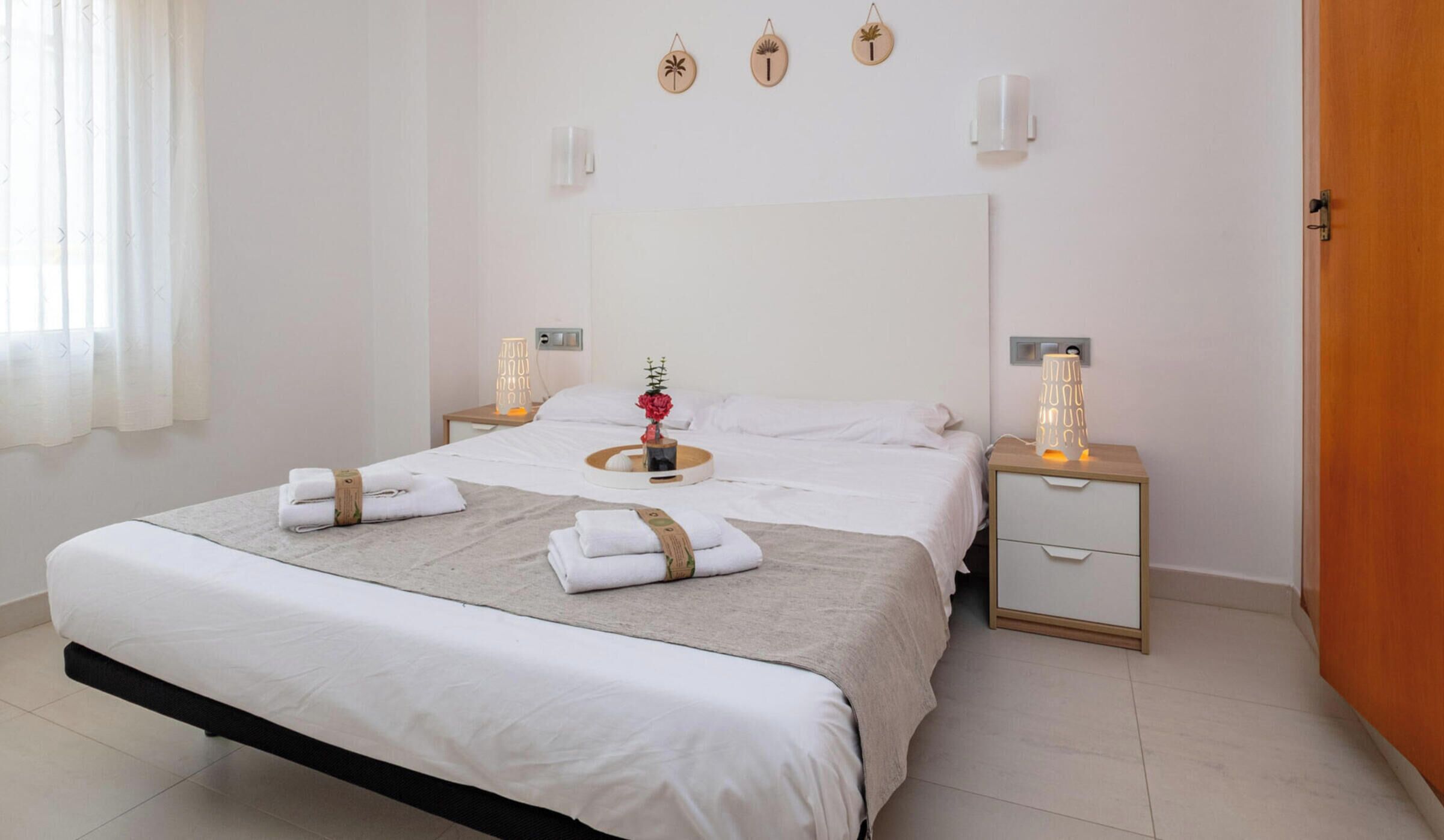 A hotel room with a large bed, two bedside tables, a nightstand, and a wooden door.