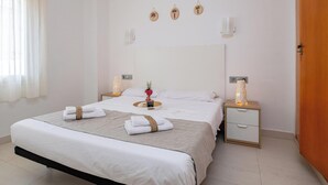 A hotel room with a large bed, two bedside tables, a nightstand, and a wooden door. - Beachfront Family Retreat with Stunning Sea Views in Palamós (Palamós)