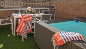 A poolside area with a wicker sofa, a dining table set with plates and glasses, and a decorative vase with flowers. - Beachfront Family Retreat with Stunning Sea Views in Palamós (Palamós)