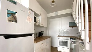 Kompakti keittiö, jossa on valkoiset kaapit, sisäänrakennettu mikroaaltouuni, liesi ja puinen työtaso.