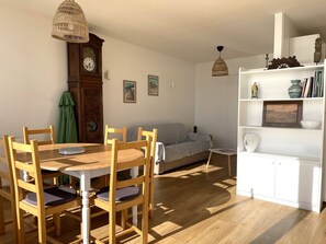 Een eetgedeelte met een houten tafel en stoelen, een bank, een boekenkast en een wandklok.