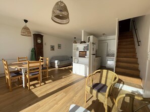 Een ruime woonkamer met een eettafel, stoelen, een bank, een boekenkast en een trap.