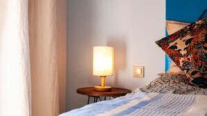 A neatly made bed with patterned pillows, a bedside lamp, and a small round table.