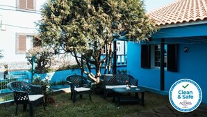 Ein blaues Haus mit Baum im Garten, einer Bank und einem Zaun.