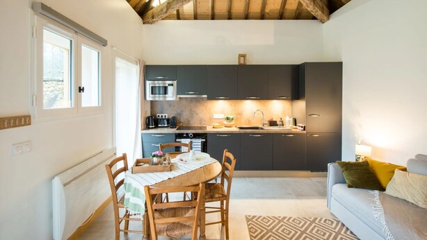 A compact kitchen with dark cabinets, a microwave, and a sink. There is a dining area with a table and chairs, and a sofa in the living area. - Château de la Malmaison (103859379) (Aÿ-Champagne)