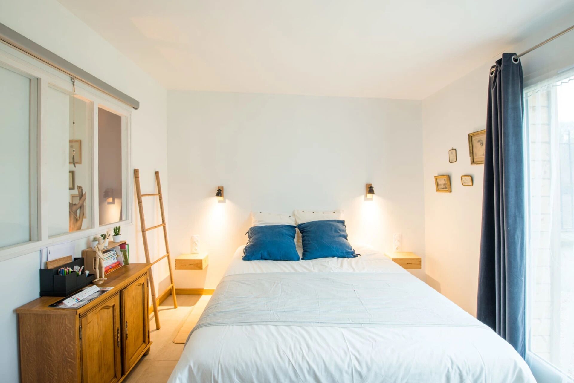Un dormitorio con cama, cómoda de madera, lámparas de noche y ventana con cortinas.