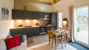 A modern kitchen with dark cabinets, a stainless steel microwave, and a dining area with a wooden table and chairs. - Château de la Malmaison (103859379) (Aÿ-Champagne)