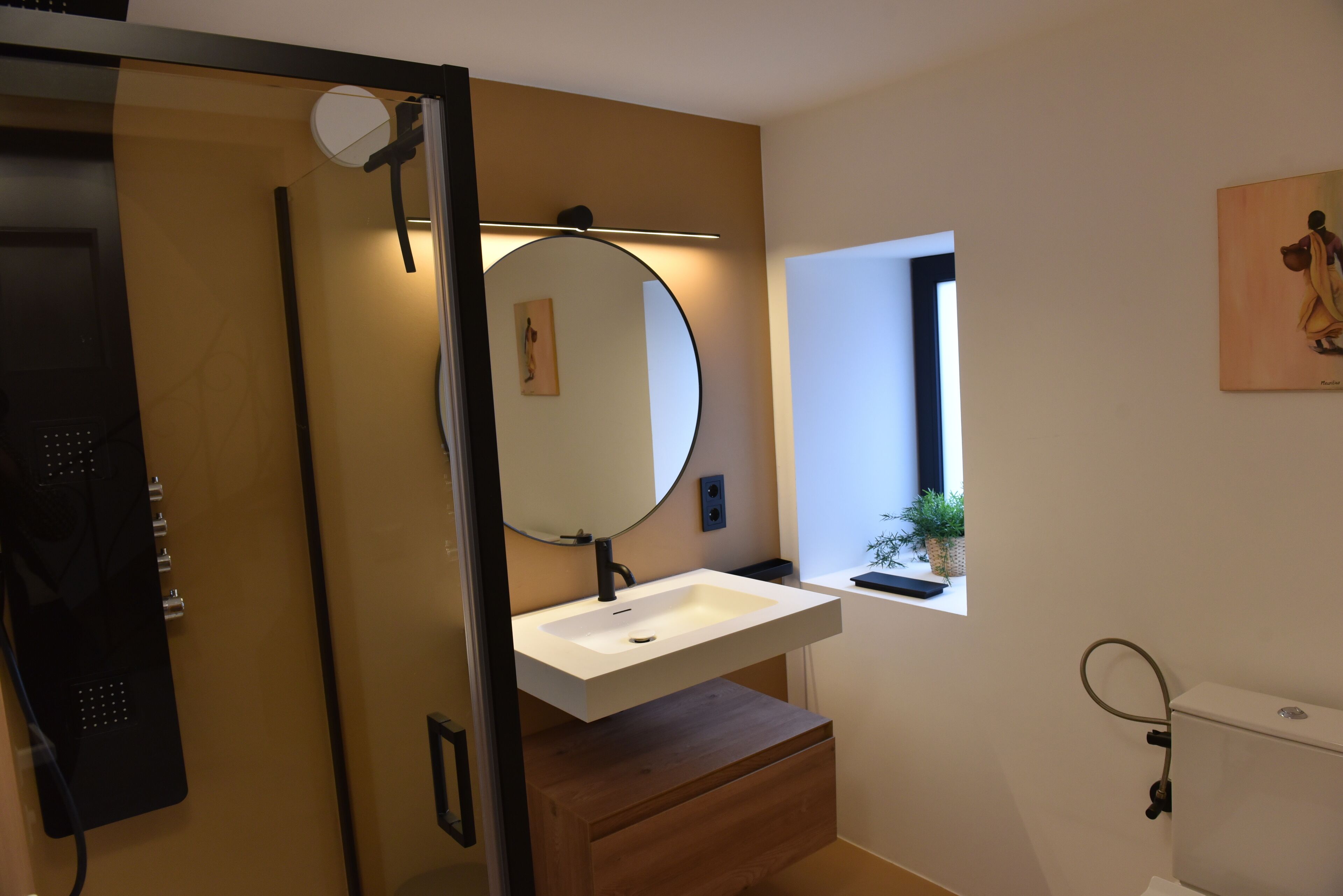 Een badkamer met een witte wastafel, een ronde spiegel en een houten wastafelmeubel.