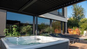Ein moderner Außenbereich mit Whirlpool, Holzterrasse, Liegestühlen und einer gläsernen Veranda.