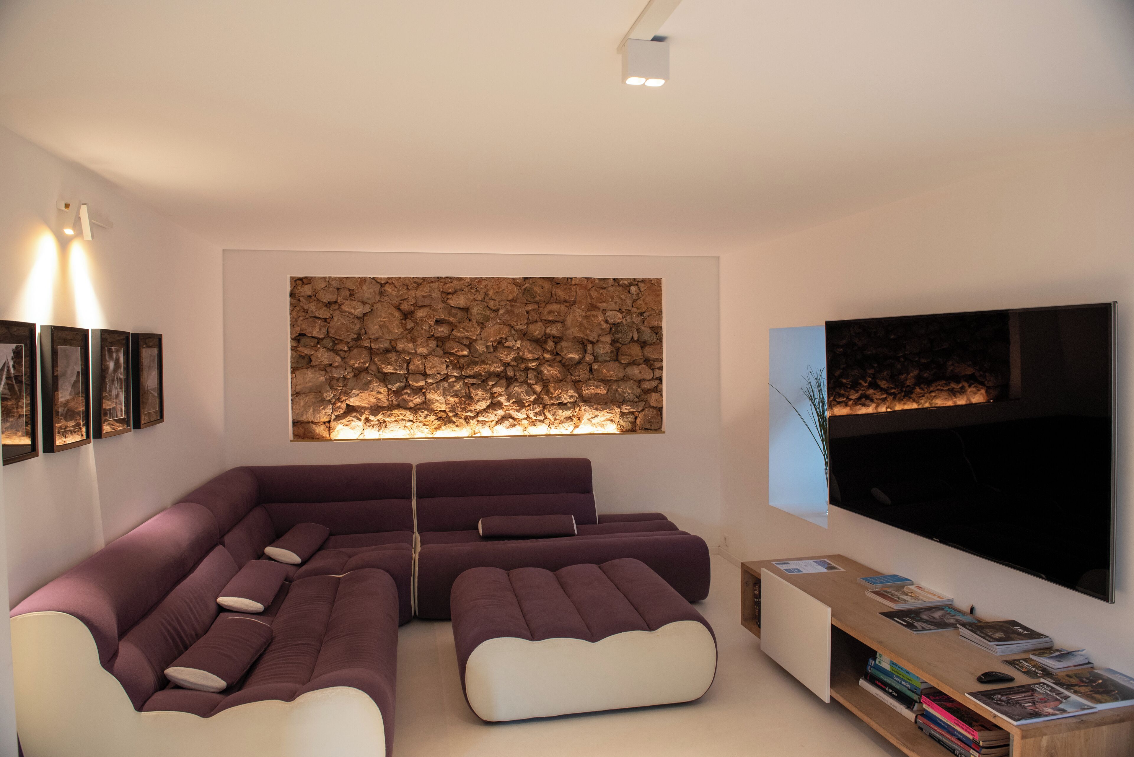 A modern living room with a sectional sofa, a stone wall feature, a flat-screen TV, and a bookshelf.