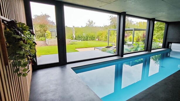 Ein Hallenbad mit großen Fenstern, Blick auf einen Garten und modernem Design.