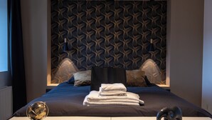 Ein modernes Hotelzimmer mit einem gemusterten Kopfteil, einem ordentlich bezogenen Bett mit Handtüchern sowie einem dekorativen Globus und einer Elefant-Figur auf dem Nachttisch.
