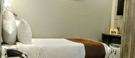 Una habitación de hotel moderna con estructura de cama de madera, ropa de cama blanca, teléfono en la mesita de noche y una obra de arte colgada en la pared.