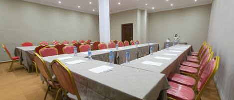 Un salón de conferencias con una larga mesa, sillas rojas y botellas de agua.