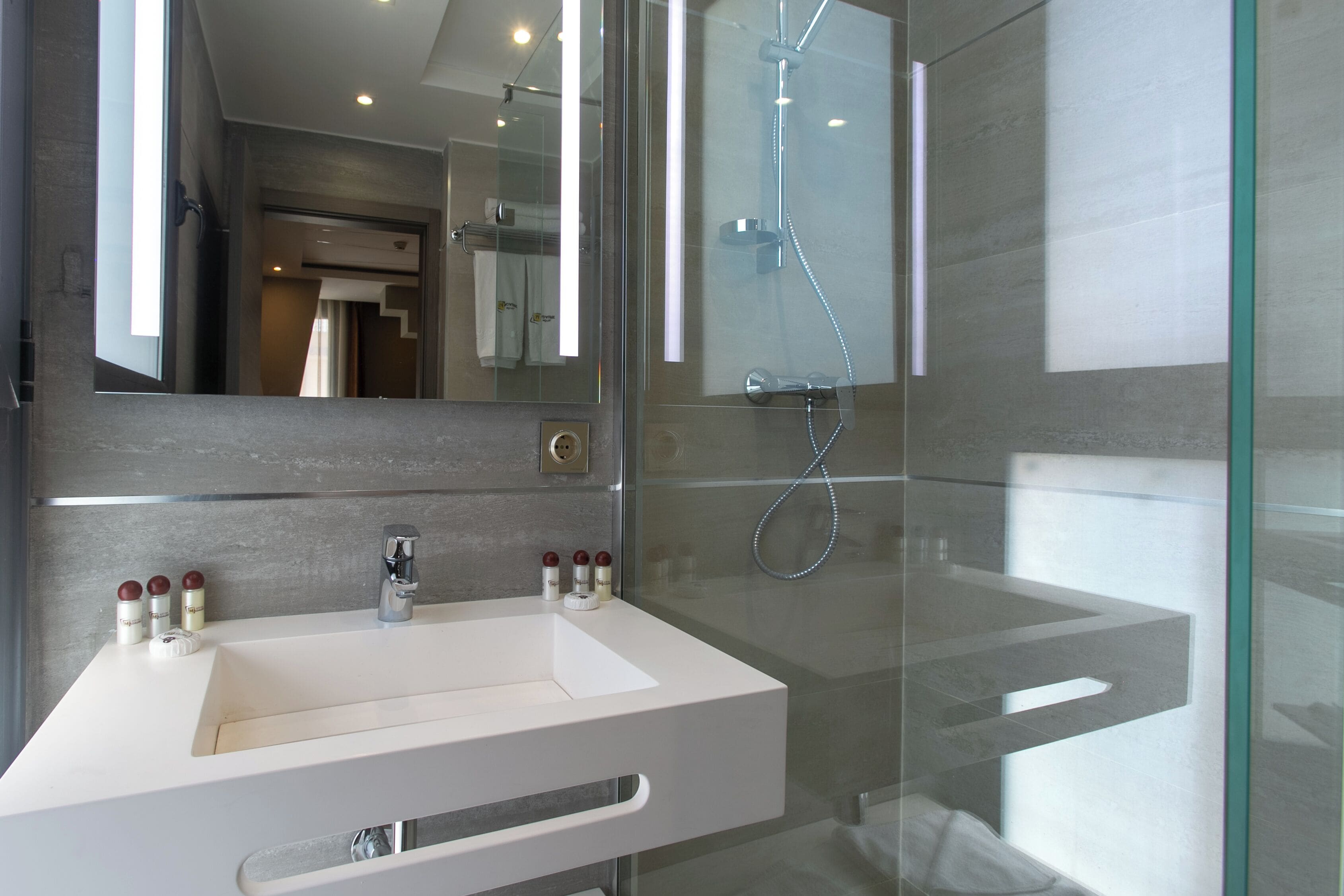 A modern bathroom with a white sink, glass shower enclosure, and a large mirror.